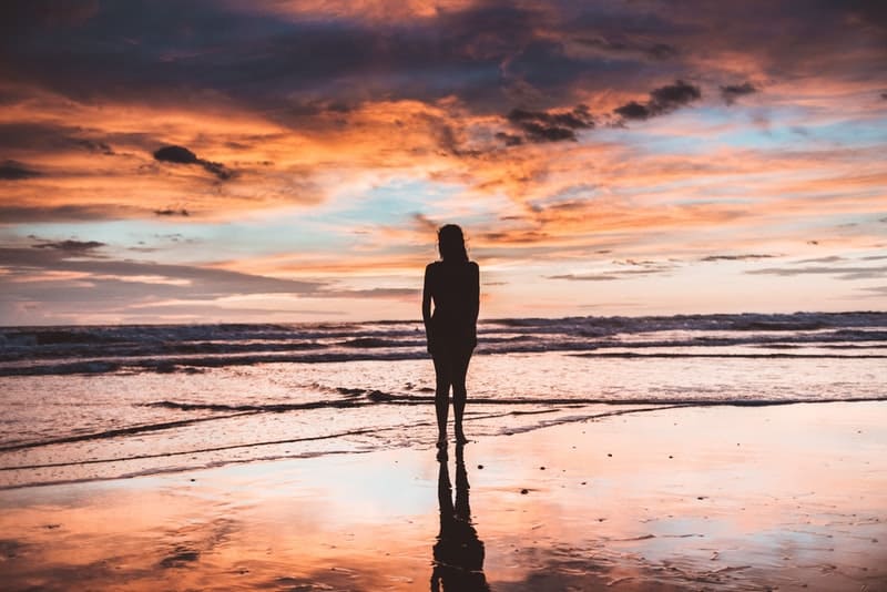 sagoma di donna in piedi davanti a uno specchio d'acqua durante l'ora d'oro