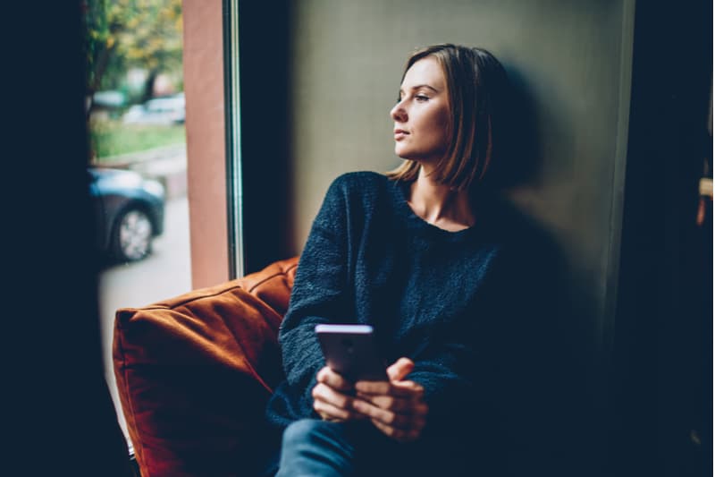 thoughtful young woman wearing black casual sitting and holding a smartphone