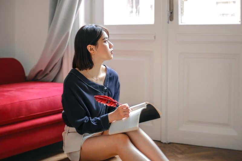 mujer pensativa escribiendo en un cuaderno en casa sentada en el suelo cerca de la puerta