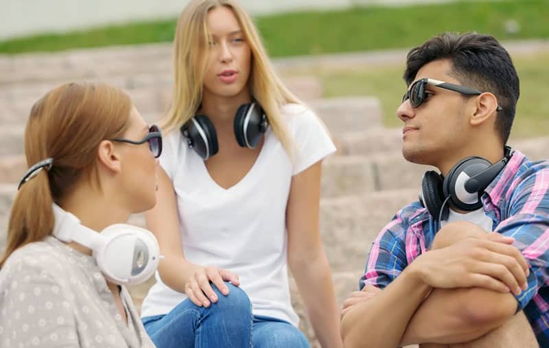 three friends chatting outdoors with headphones hanging on their neck