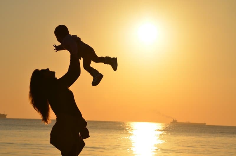 woman carrying baby at the beach during sunset/sunrise