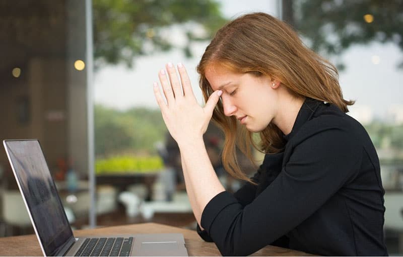 woman closing eyes facing the laptop outdoors