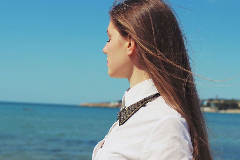 mujer cerrando los ojos frente a la masa de agua en una vista lateral