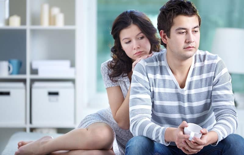 mujer consolando a un hombre disgustado sentado en el sofá dentro de la sala de estar