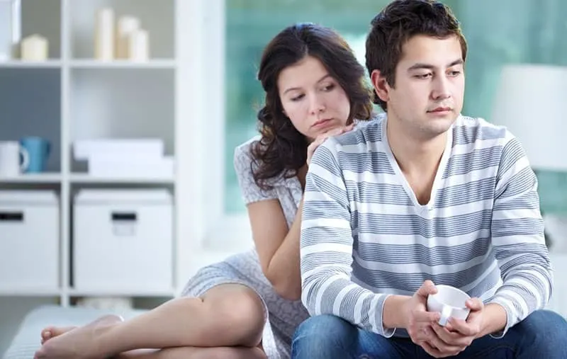 woman consoling an upset man sitting on couch inside living room