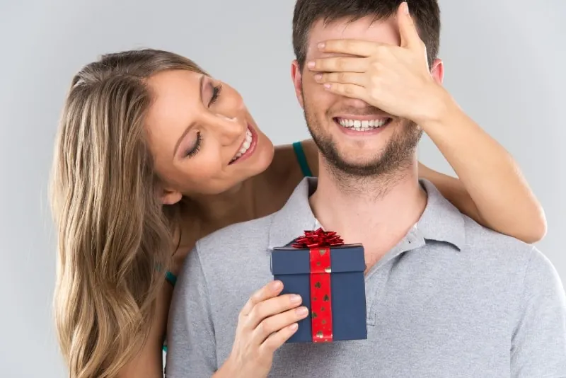 woman covering man's eyes while giving him gift