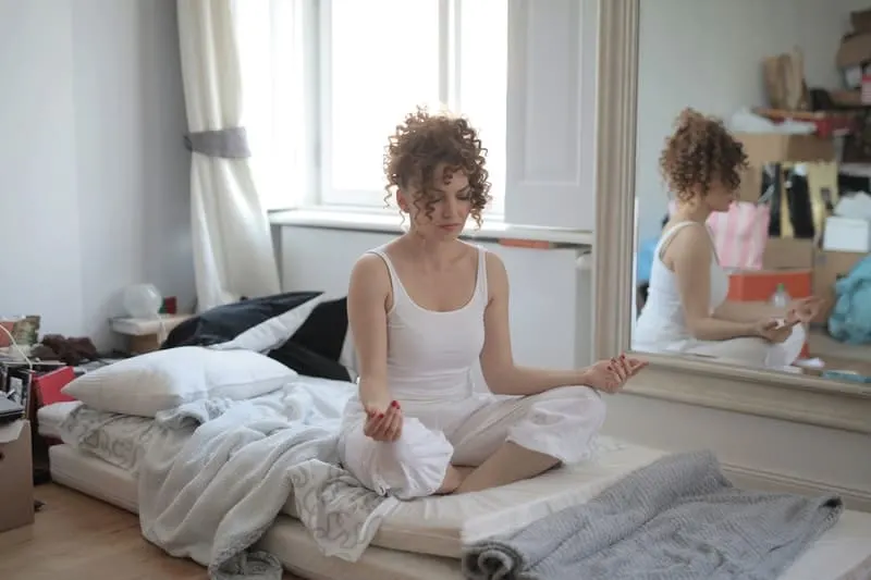 woman doing a lotus pose on bed after waking up