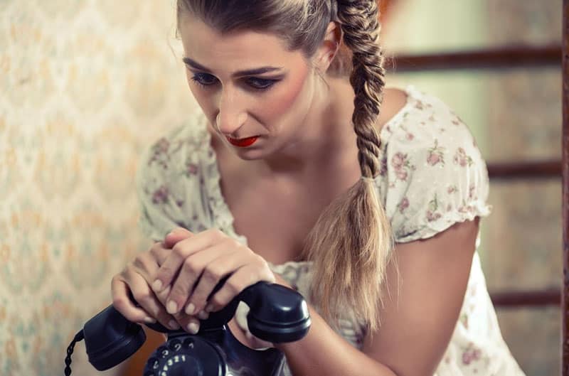 mujer sosteniendo un telefono viejo levantandolo vestida con el pelo trenzado