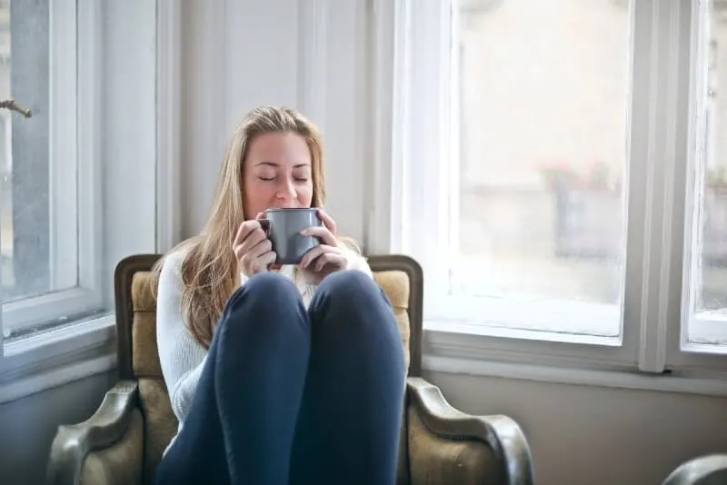 woman holding mug while sitting near window