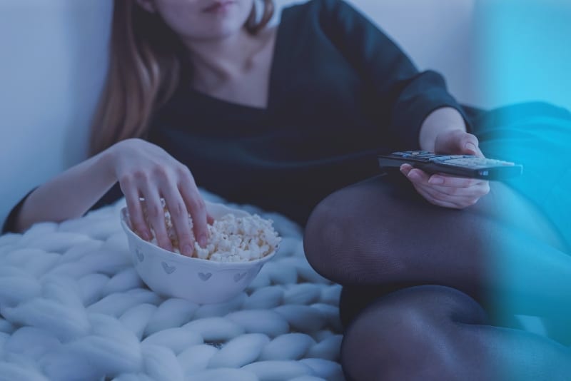 woman holding remote control while eating popcorn