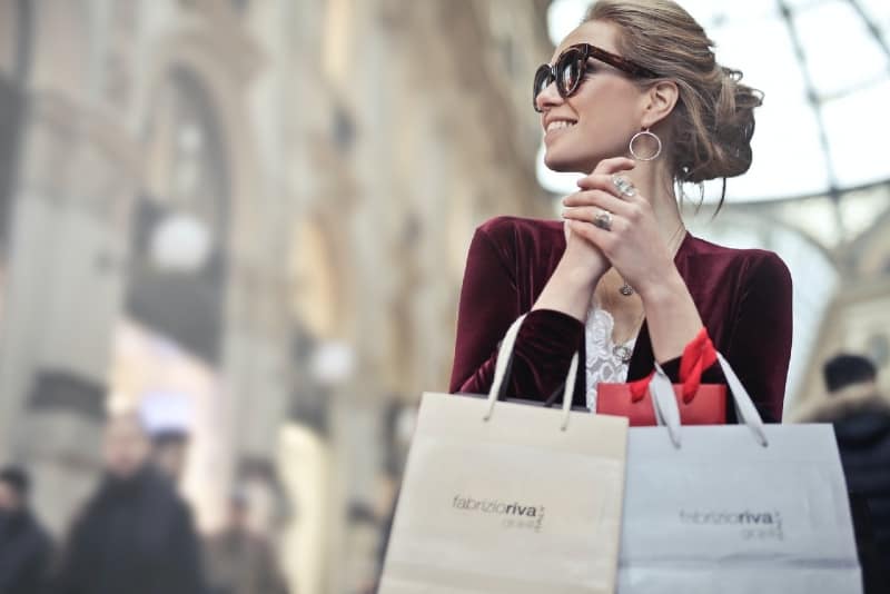 donna sorridente con occhiali da sole che tiene in mano borse della spesa 