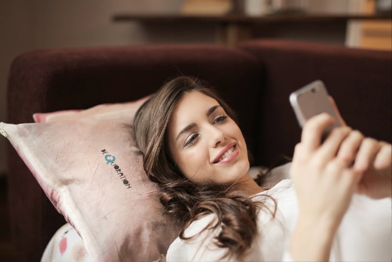 donna sorridente che tiene in mano uno smartphone mentre è sdraiata sul divano