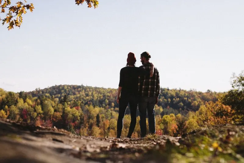 woman hugging man while standing near green trees