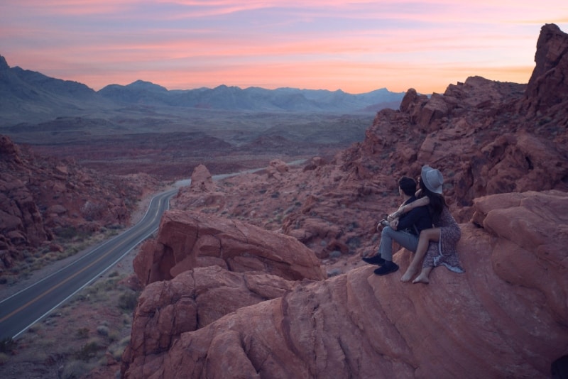 woman hugging man while sitting on rock during sunset