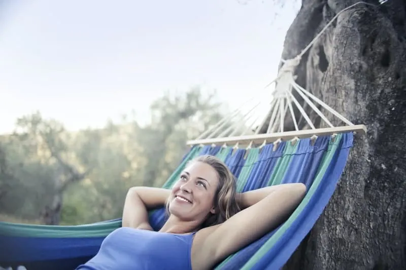 woman in blue tank top lying on a hammock from a tree