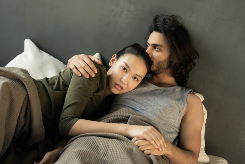 woman in green top lying and cuddling beside a man in bed