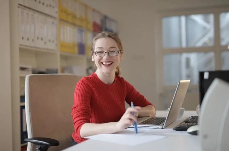 woman in red sweater leaning on white table smiling in the office