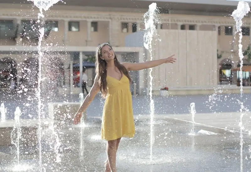 woman in yellow sleeveless dress standing in the middle of the park's fountains