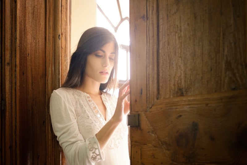 woman in white shirt leaning on brown door frame