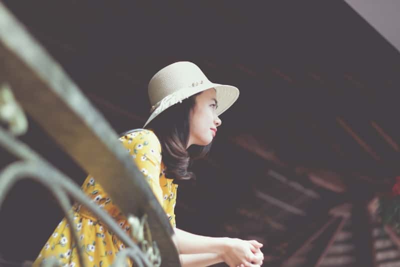 mujer con sombrero apoyada en una valla