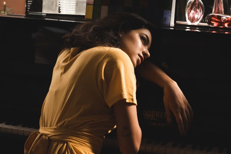 woman in yellow dress leaning on piano