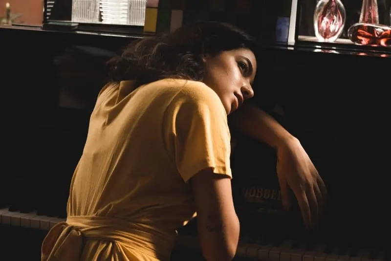 woman in yellow dress leaning on piano