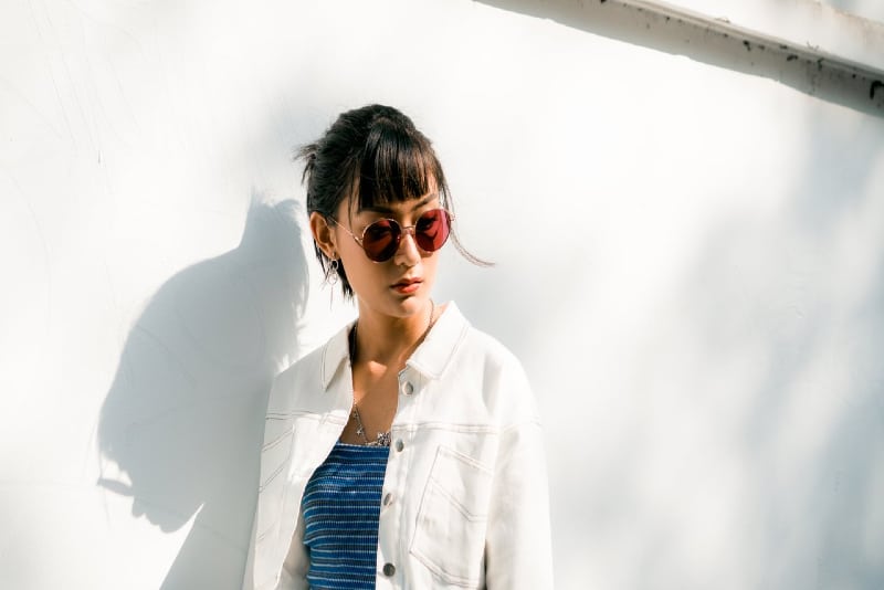 mujer con gafas de sol apoyada en una pared blanca