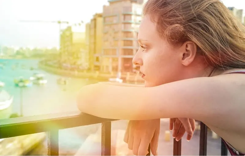 woman leaning over railings and thinking with rainbow color shining thru the picture