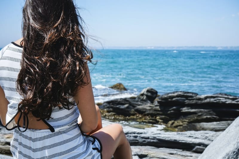 mulher de vestido preto e branco a olhar para o mar