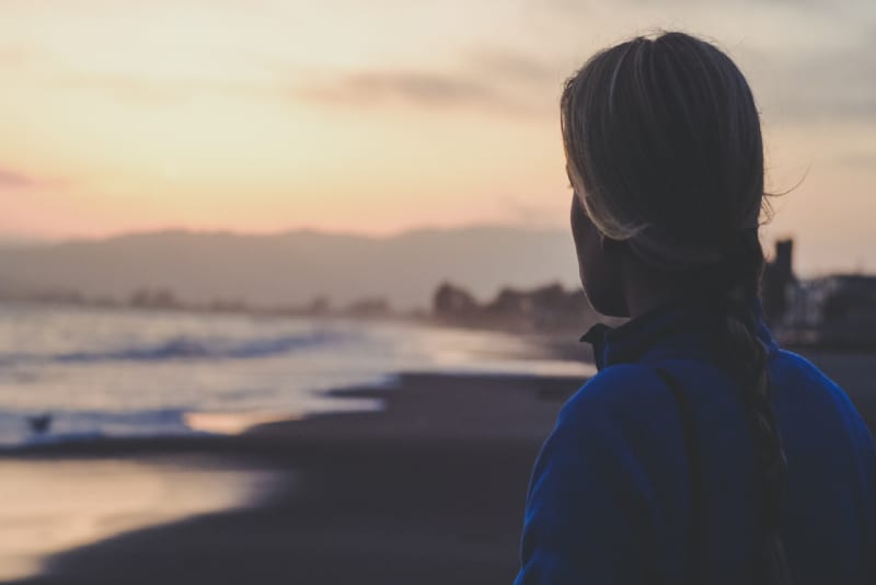 woman in blue jacket looking at sea during sunrise