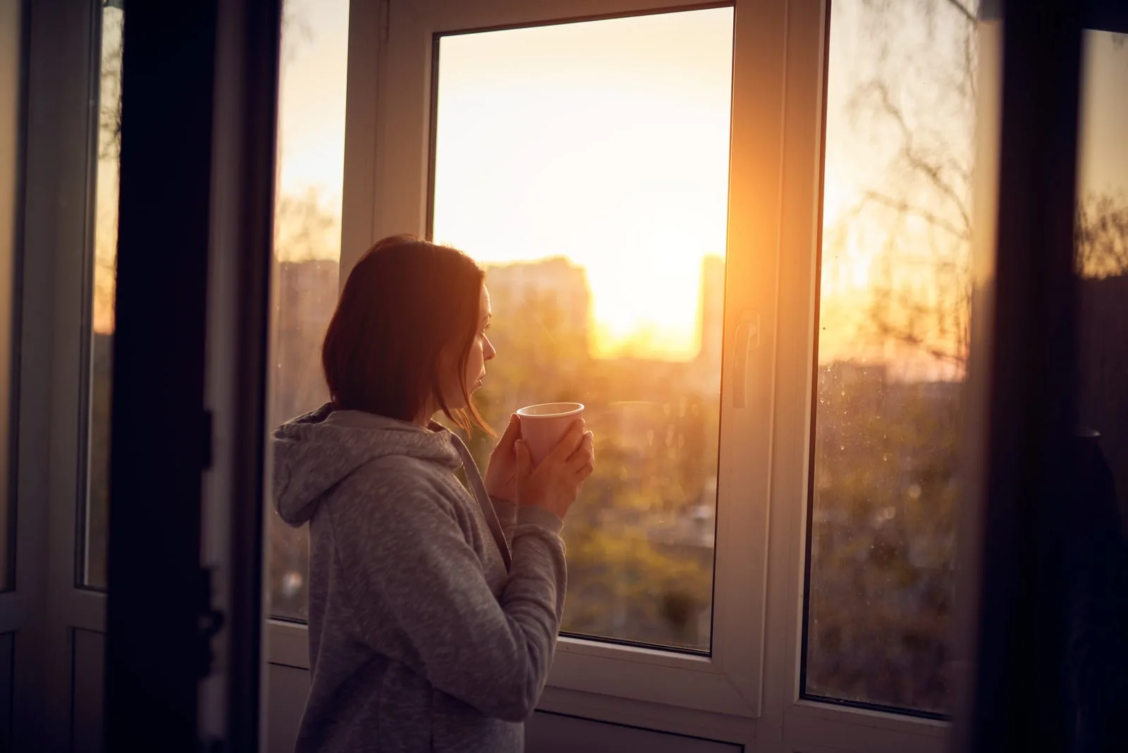 woman holding cup of tea and looking out of window
