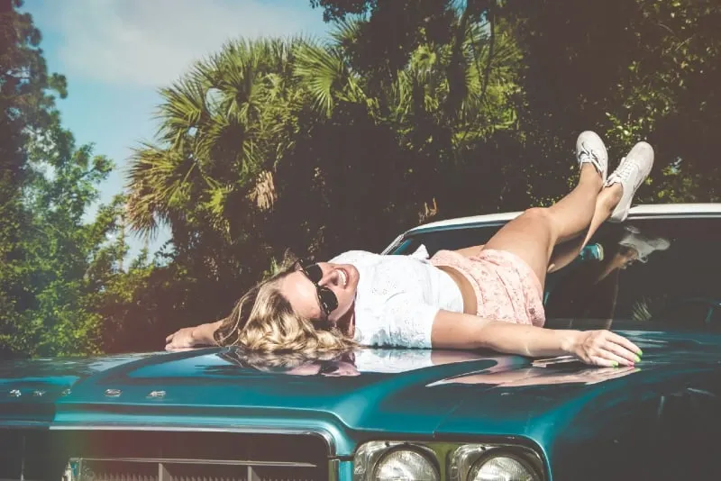 blonde woman with sunglasses lying on car