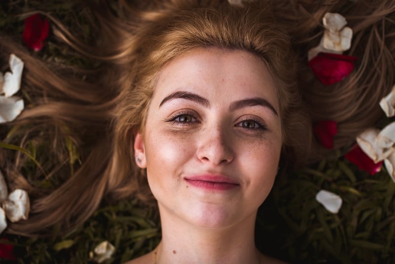 mujer sonriente con pintalabios rojo tumbada en la hierba