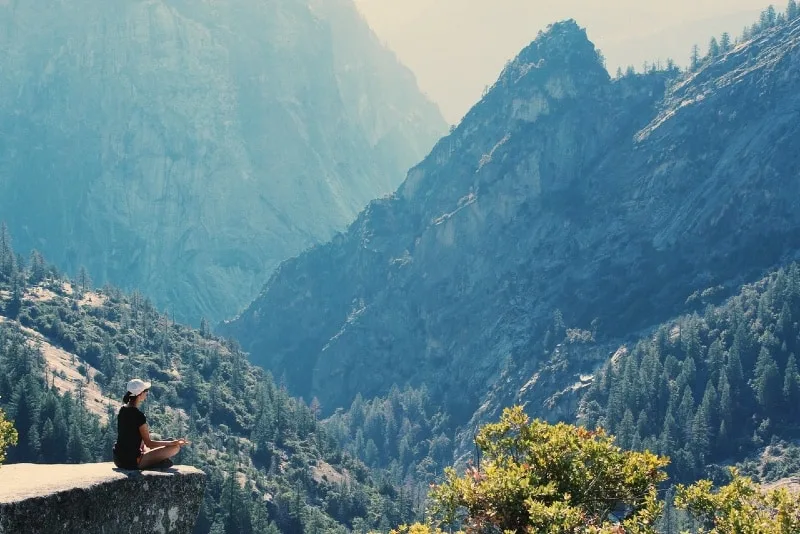 woman meditating while sitting on cliff near mountain