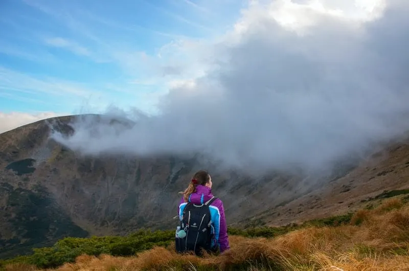 woman on mountain peak carrying hiking backpack facing the thick clouds