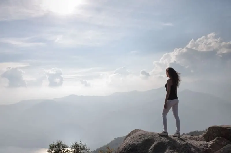 woman on top of the mountain with sun shining, woman wearing white jeans