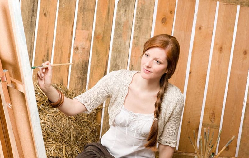 woman painting in canvass looking at her subject somewhere inside a barn