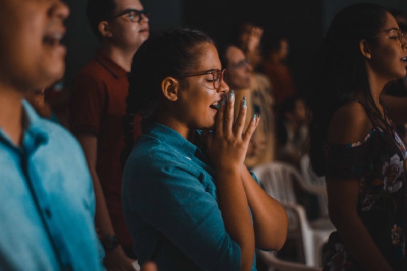 woman in blue shirt with eyes closed praying