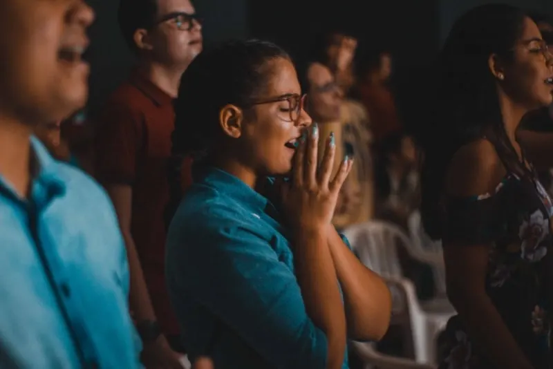 woman in blue shirt with eyes closed praying