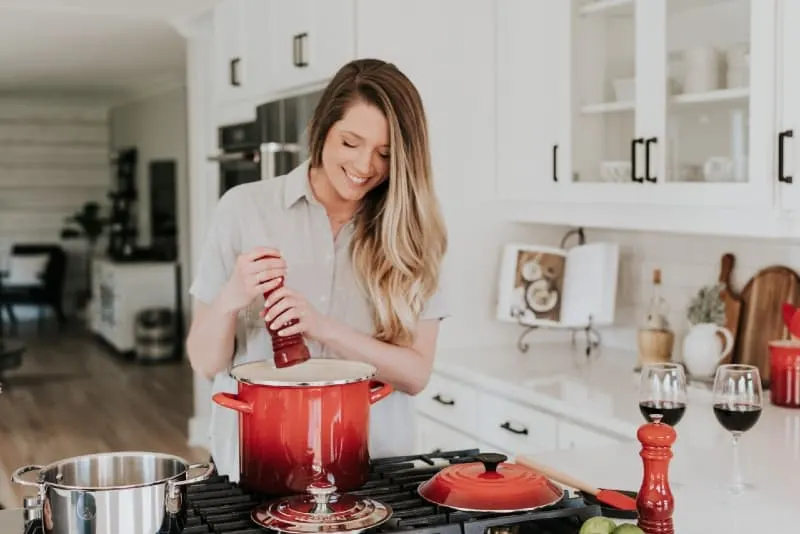 woman putting pepper on stock pot while standing in kitchen