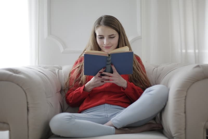 woman reading book while sitting on sofa