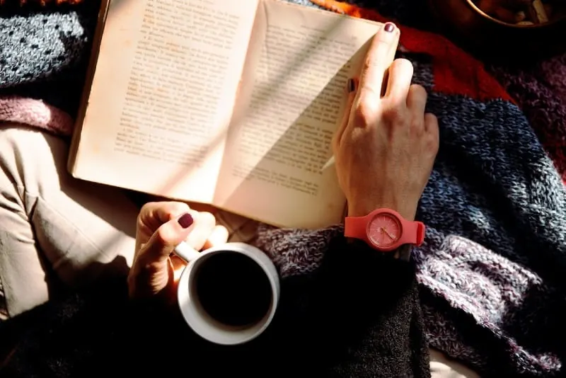 woman holding mug while reading book