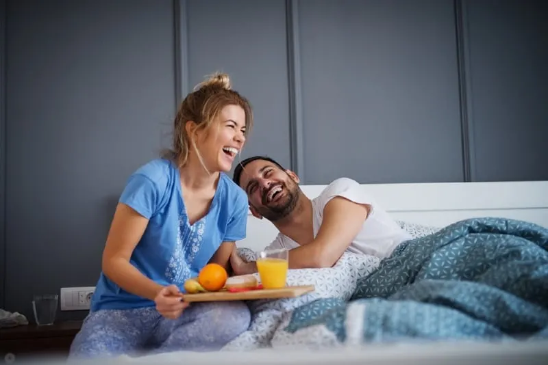 smiling woman serving breakfast to man in bed