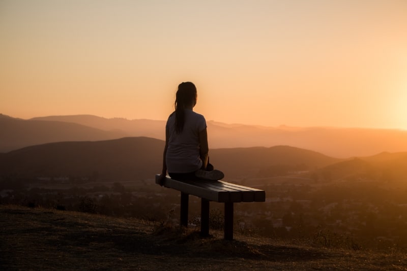 woman sitting on bench looking at mountain during sunset