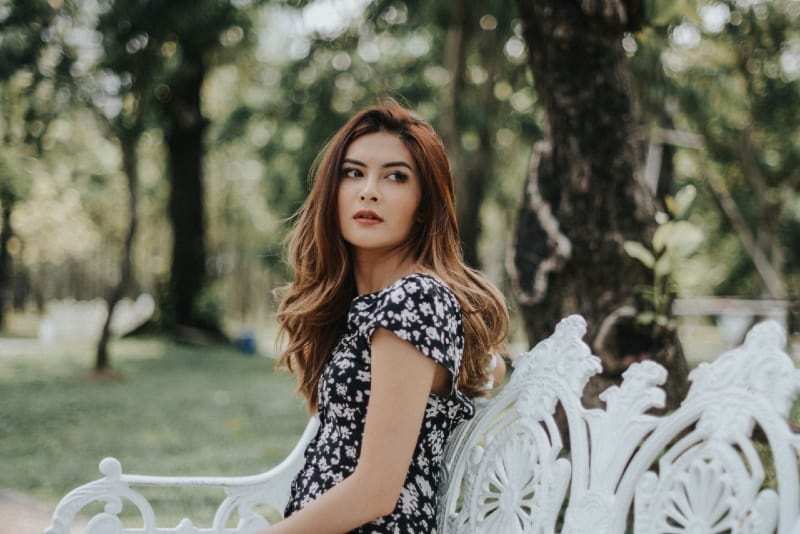 mujer con vestido de flores sentada en un banco blanco