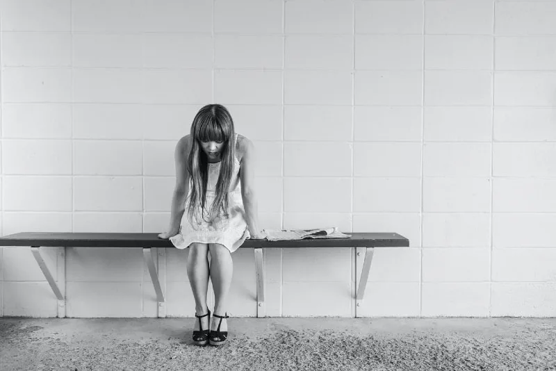 sad woman sitting on bench near wall