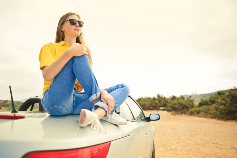 woman in yellow t-shirt sitting on silver car