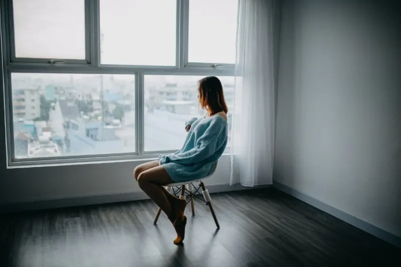 woman in blue sweater sitting on chair near window