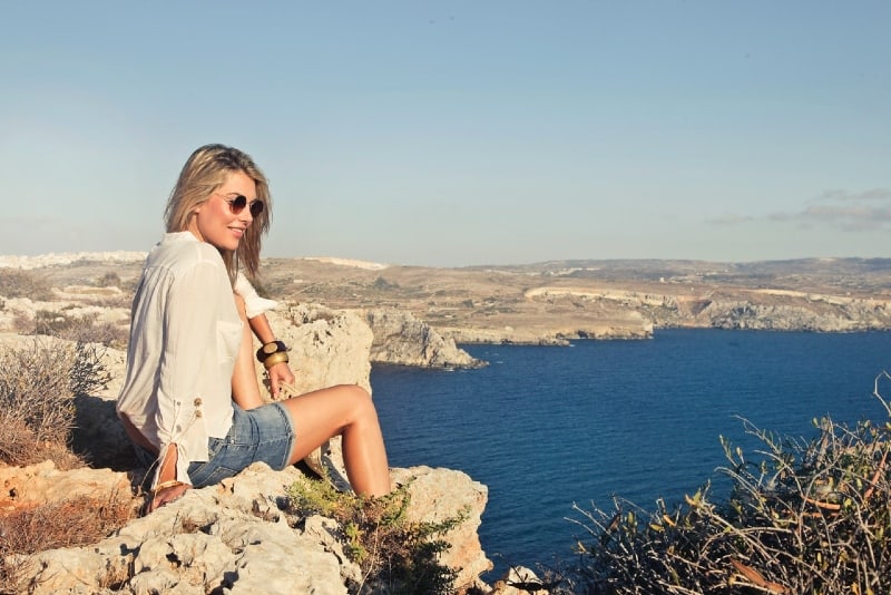 smiling woman with sunglasses sitting on cliff