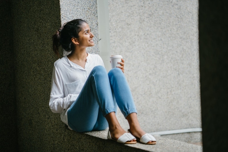 mulher sorridente de camisa branca sentada numa superfície de betão